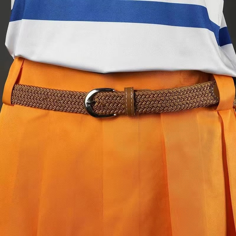 A close-up of a brown braided belt with a silver buckle worn over bright orange pleated trousers, with a white and blue striped shirt partially visible at the top.