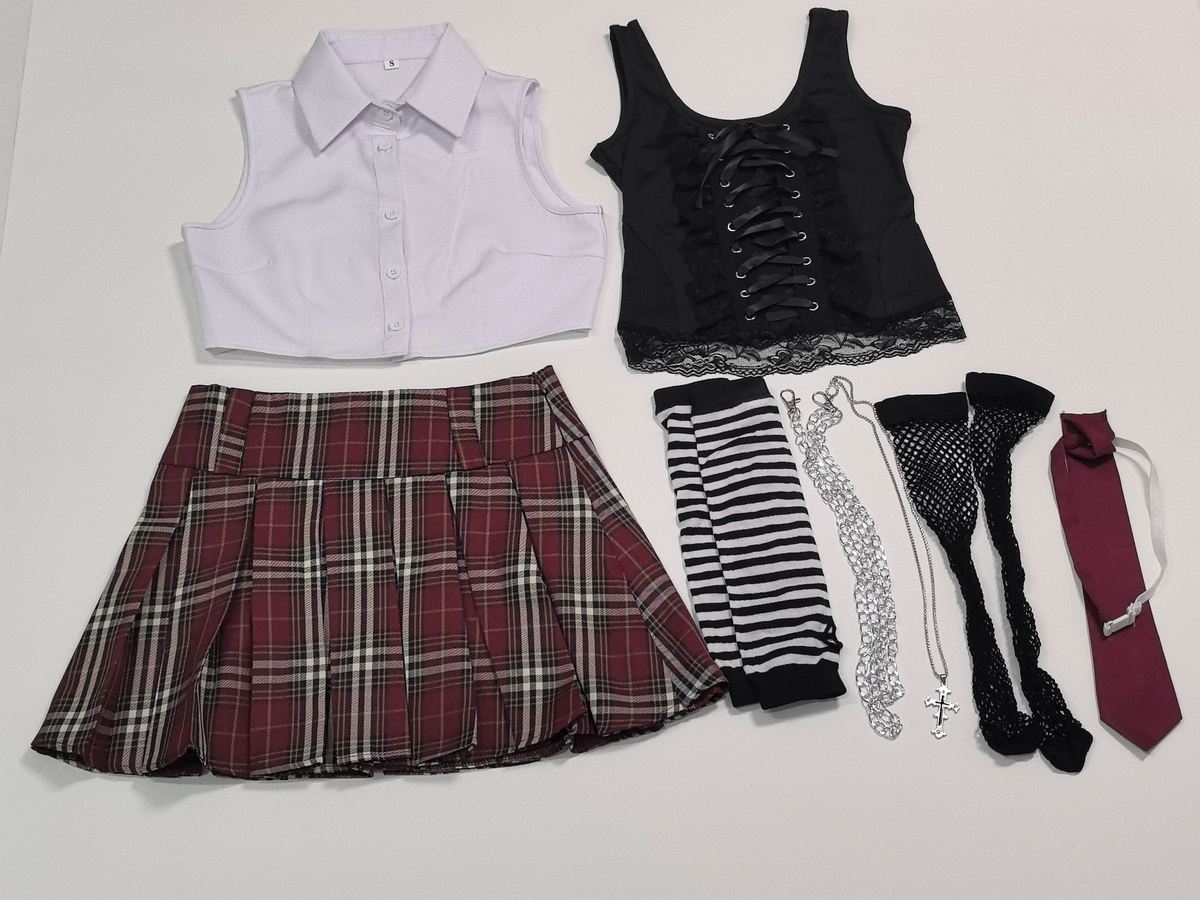 A flat-lay of a gothic schoolgirl costume set on a white background, including a white sleeveless collared shirt, a black lace-up corset top, a red plaid pleated skirt, striped tights, fishnet tights, a black lace skirt, a silver chain necklace, and a burgundy necktie.