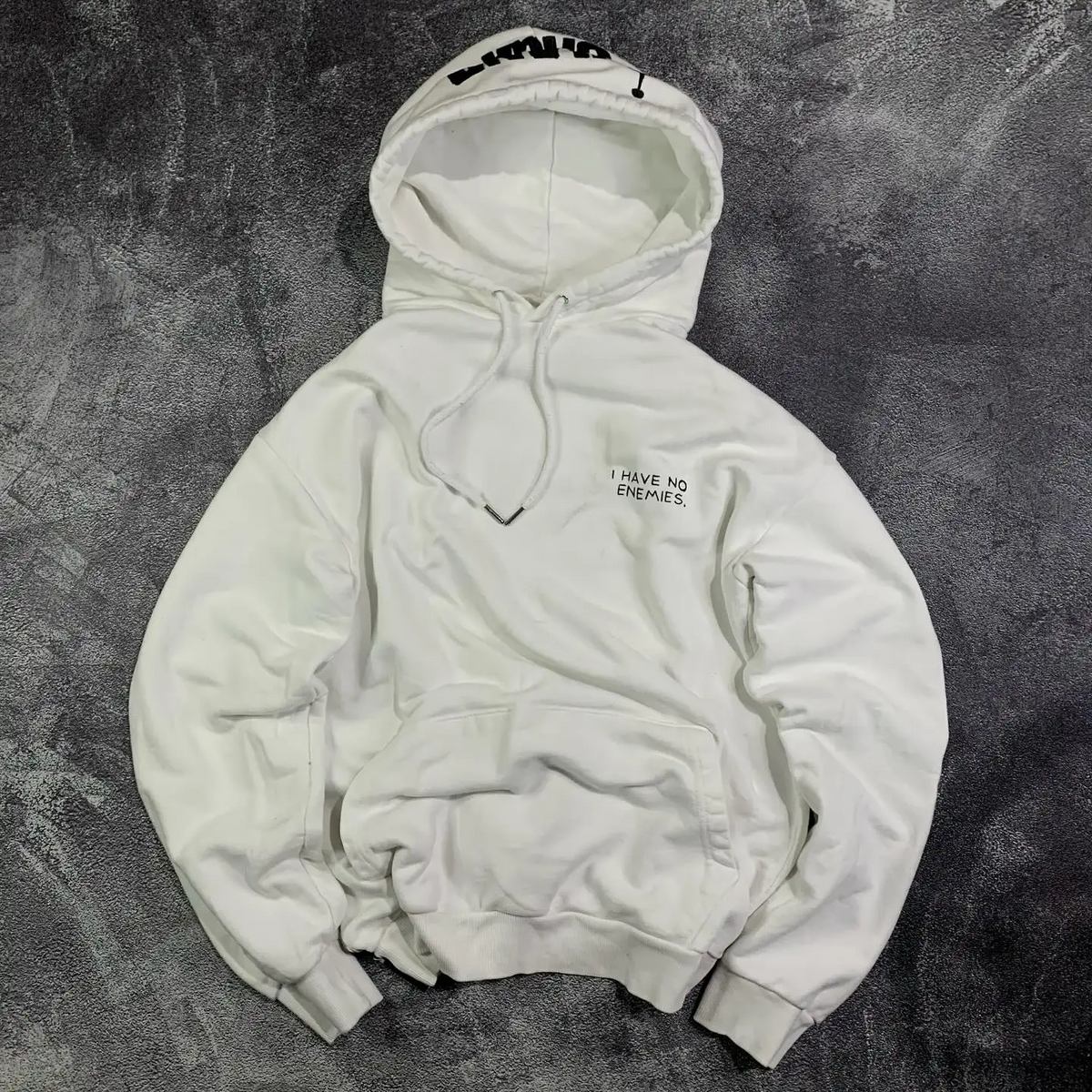 Front view of a white oversized heavyweight pullover hoodie featuring minimalist 'I have no enemies' chest typography by SkaiiyPrints