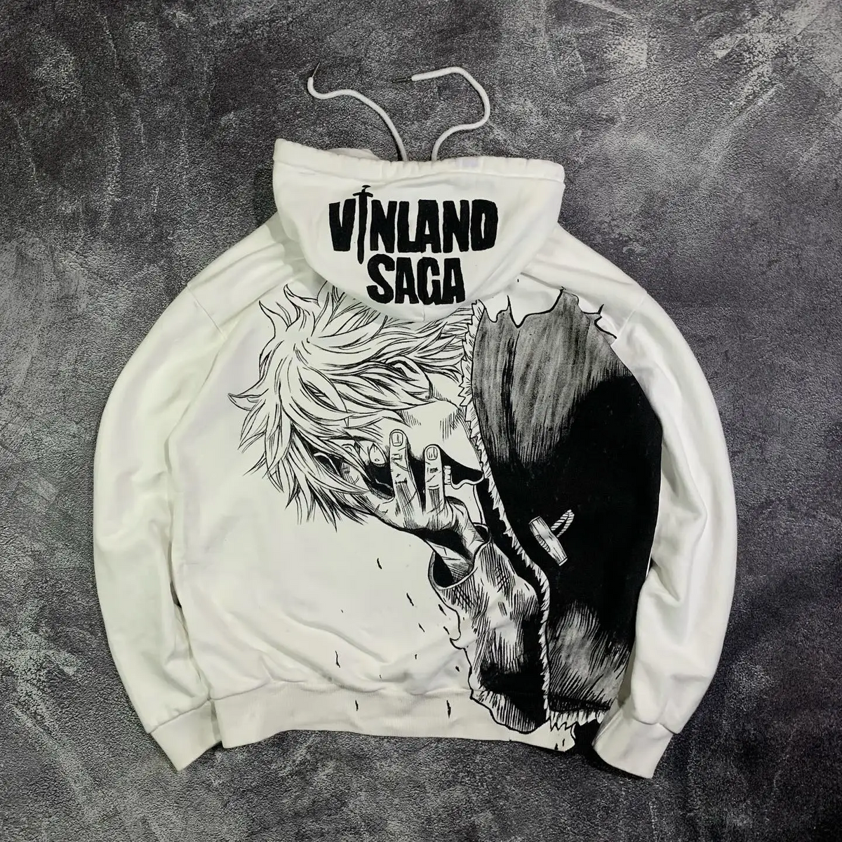 Flat lay of the back of a white streetwear hoodie featuring a massive Thorfinn manga portrait graphic and a printed hood.