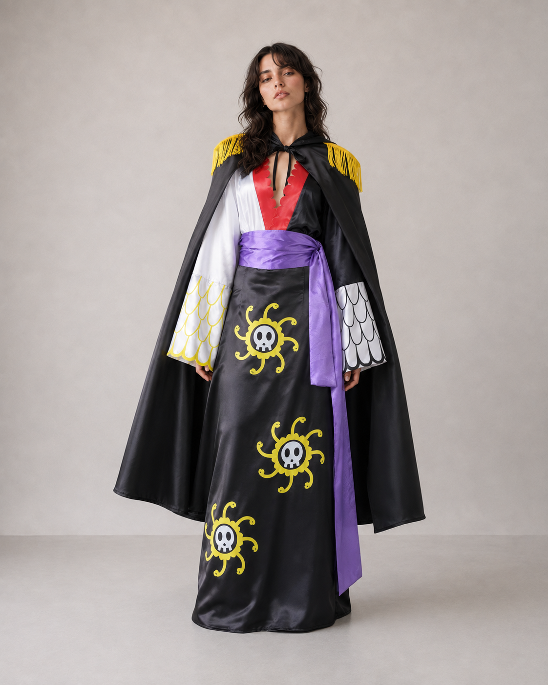 A model wearing a pirate-themed costume dress with a black skirt featuring yellow skull-and-crossbones designs, a purple sash, a white and red V-neck bodice, and a black cape with yellow trim and patterned sleeves, set against a plain light gray studio background.